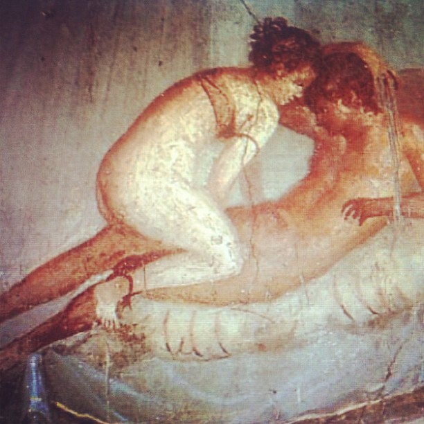 Pintura mural antigua de dos cuerpos desnudos abrazados sobre un lecho