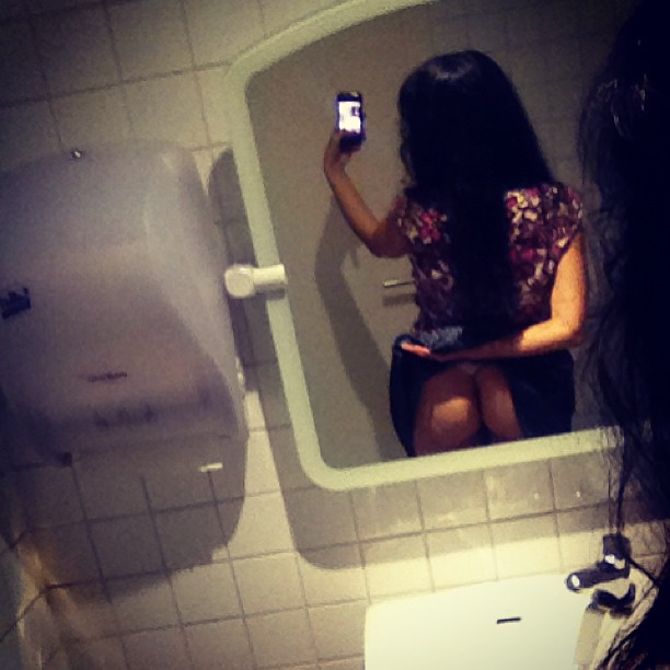 Autorretrato de Roser Amills de espaldas en el espejo de un lavabo, con el móvil en la mano