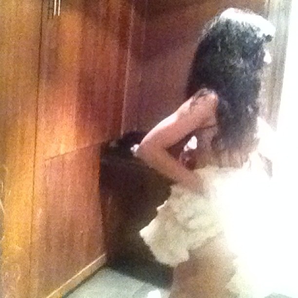 Roser Amills, de espaldas junto a una puerta de madera, con un vestido blanco de volantes