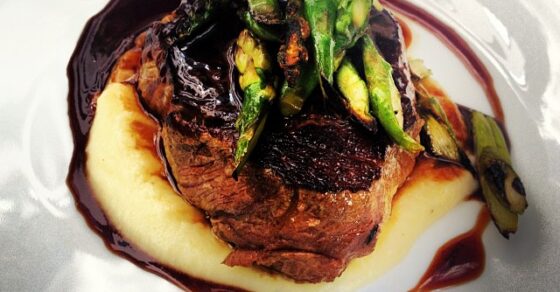 Plato de carne con puré de patata, salsa oscura y espárragos