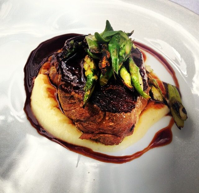 Plato de carne con puré de patata, salsa oscura y espárragos