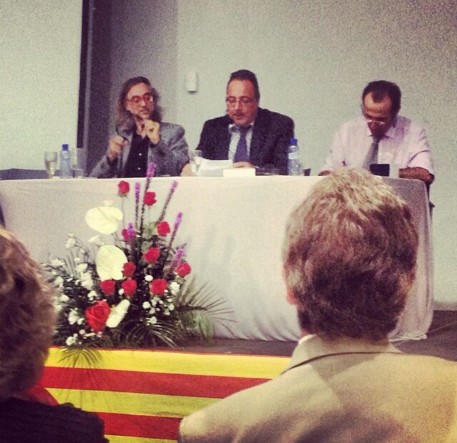 Tres ponentes en la mesa de clausura de la Jornada d'Estudis Càtars de Bagà, con Victor Amela a la izquierda, ante una senyera y un ramo de flores