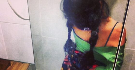 Foto de Amills Public WC: una mujer de espaldas, con trenzas, ante el espejo de un cuarto de baño