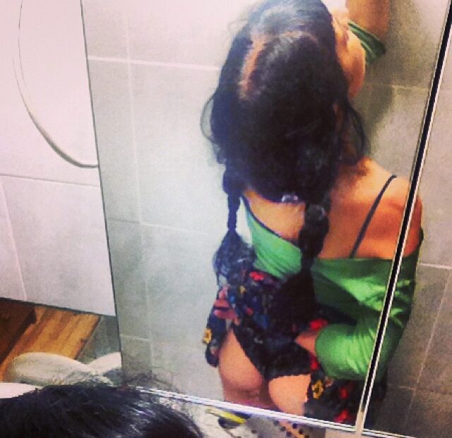 Foto de Amills Public WC: una mujer de espaldas, con trenzas, ante el espejo de un cuarto de baño