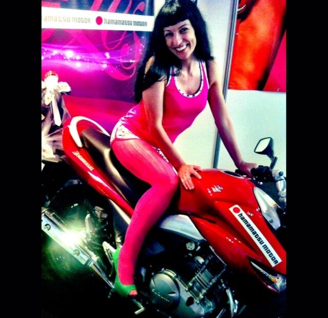 Roser Amills, con medias y camiseta rosas, sonríe sentada sobre una moto roja en el Salón Erótico de Barcelona