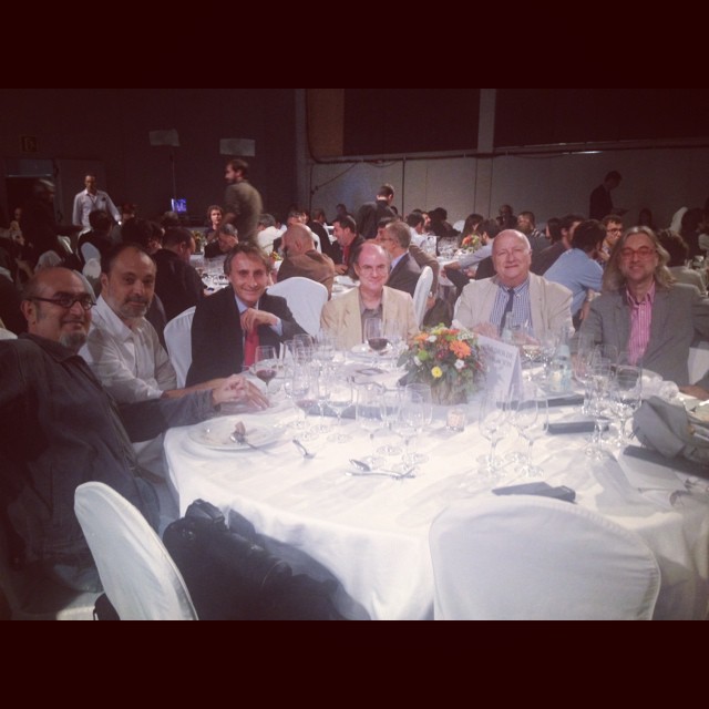 Siete hombres sentados a una mesa redonda con mantel blanco en la cena del Premio Planeta 2013; el de la derecha tiene el pelo largo y gafas