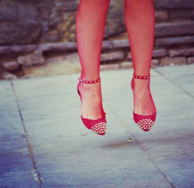 Piernas de mujer en el aire con zapatos rojos de tachuelas sobre un suelo de piedra