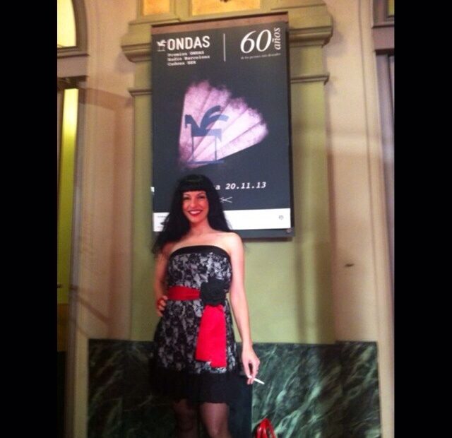Roser Amills con vestido de encaje negro y cinta roja ante el cartel de los 60 premios Ondas