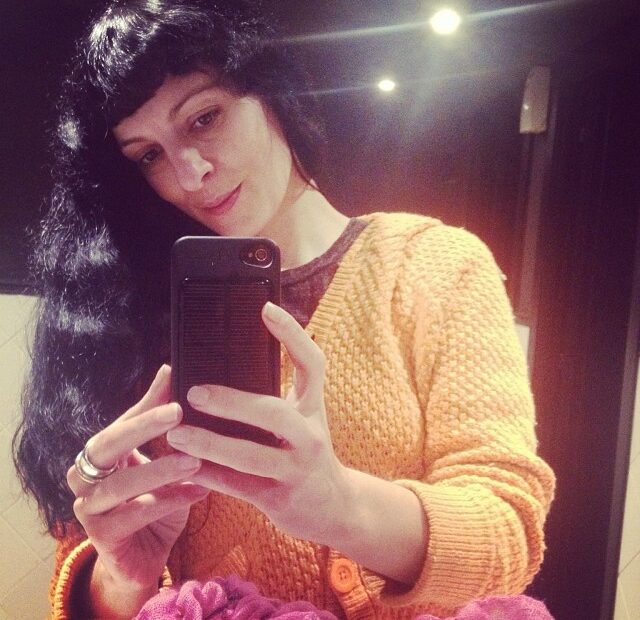 Roser Amills con jersey naranja de punto haciéndose un selfie con el móvil ante un espejo