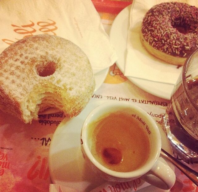 Un cronut mordido y una taza de café sobre una mesa