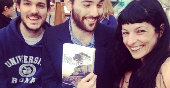 Roser Amills somriu en una terrassa amb dos amics; el de l'americana mostra un exemplar de Fes bondat