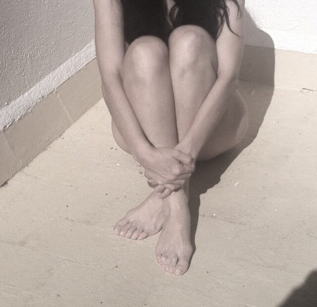 Mujer sentada en el suelo, abrazada a sus rodillas, en blanco y negro