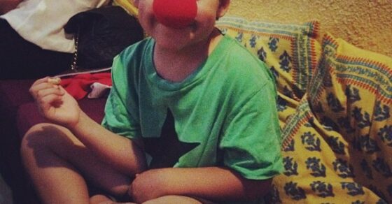 Juan, el hijo de Roser Amills, sentado con las piernas cruzadas y una nariz roja de payaso