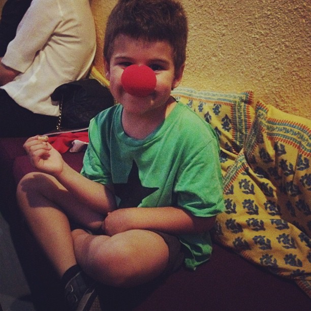 Juan, el hijo de Roser Amills, sentado con las piernas cruzadas y una nariz roja de payaso