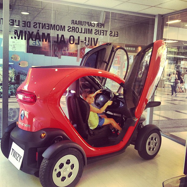 Juanito, el hijo de Roser Amills, sentado al volante de un coche eléctrico Renault Twizy rojo con las puertas abiertas hacia arriba