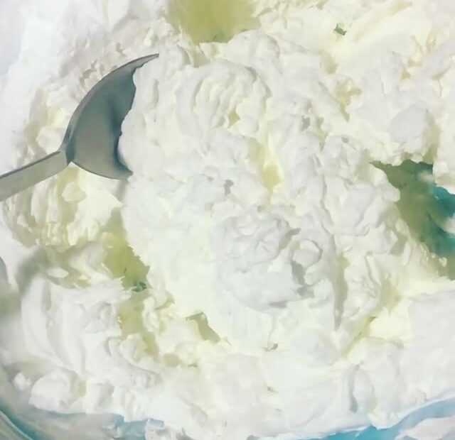 Primer plano de nata montada casera en un cuenco, con una cuchara metálica a la izquierda