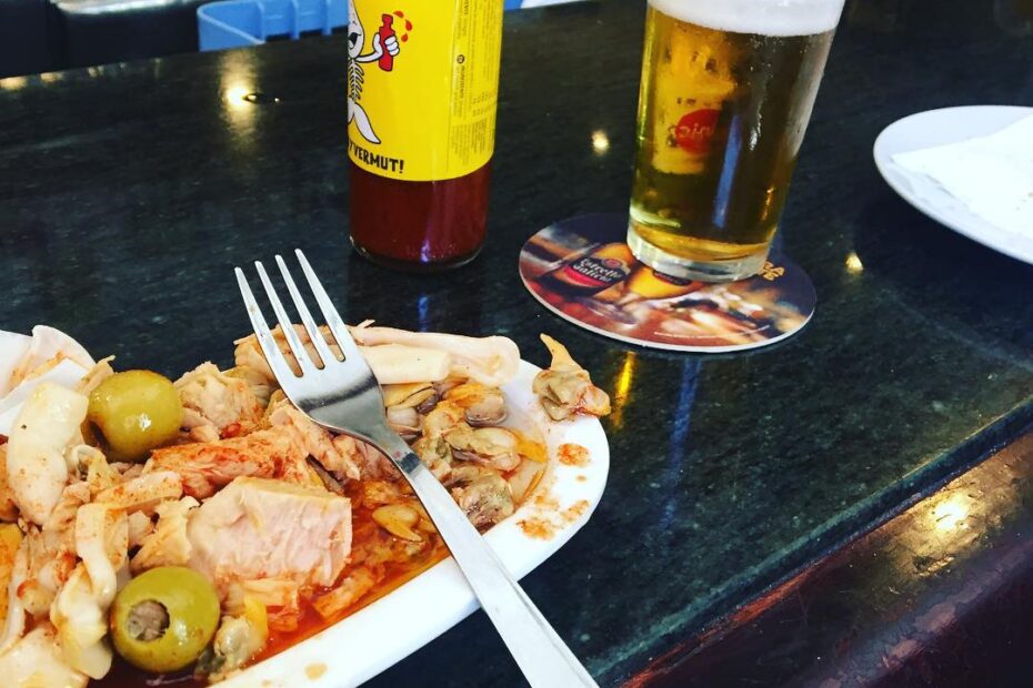Plato de aperitivo con anchoas y aceitunas, una cerveza y una botella de salsa picante en la barra de un bar
