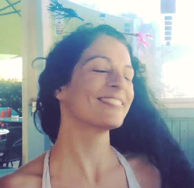 Roser Amills sonríe con los ojos cerrados y el pelo largo moviéndose, en la terraza de un chiringuito