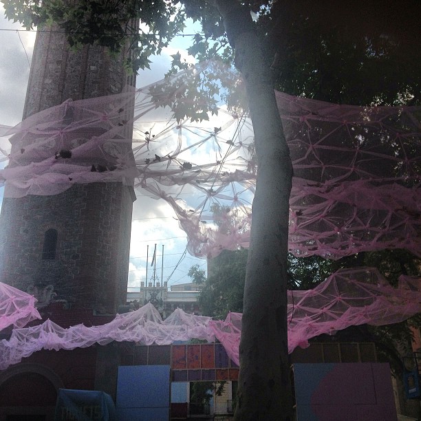 Estructuras de telarañas rosas colgadas entre árboles en una plaza del barrio de Gràcia
