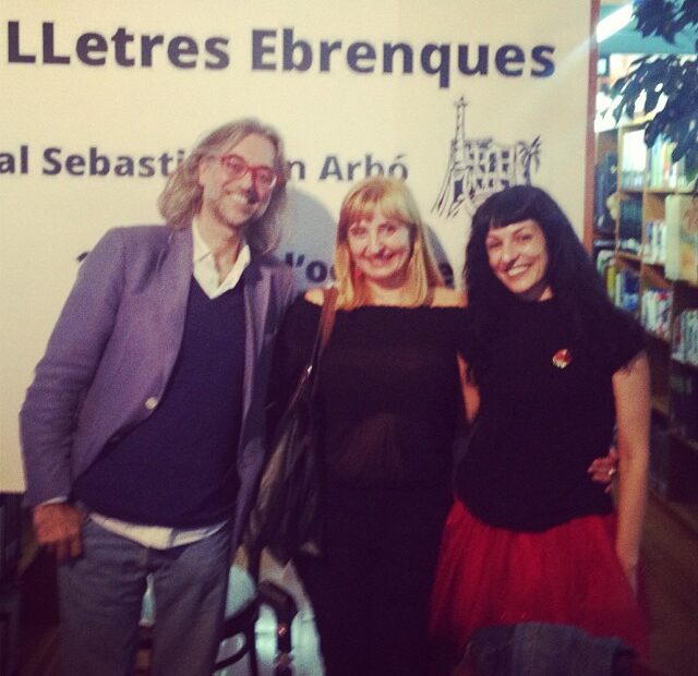Roser Amills, a la dreta, amb la Roser Reverté i un home amb ulleres vermelles davant del plafó de les Jornades de les Lletres Ebrenques, a la Biblioteca Sebastià Juan Arbó d'Amposta