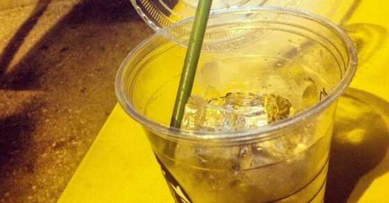 Vaso de plástico con hielo y una pajita verde sobre un banco amarillo, de noche