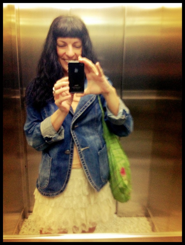 Roser Amills fent-se un selfie al mirall d'un ascensor, amb jaqueta texana, faldilla de volants i bossa verda