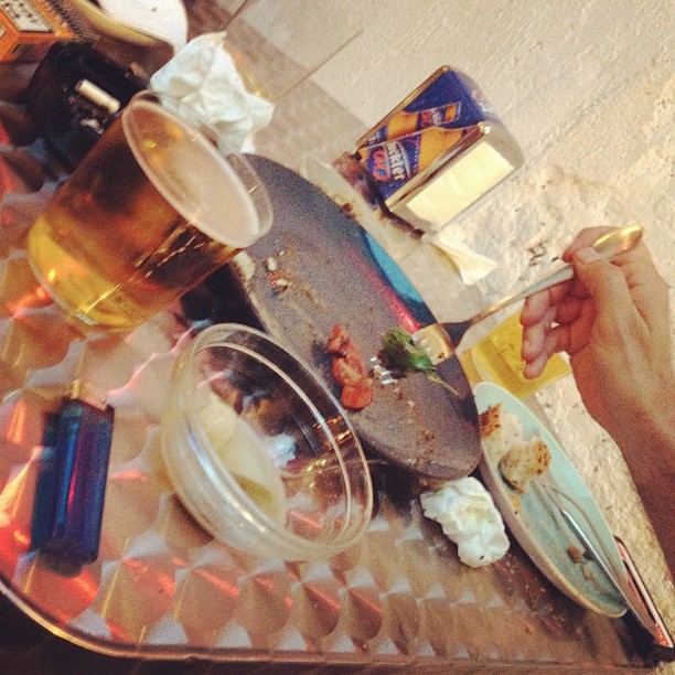 Mesa de terraza con una jarra de cerveza, platos con restos de comida, una caja metálica y un mechero
