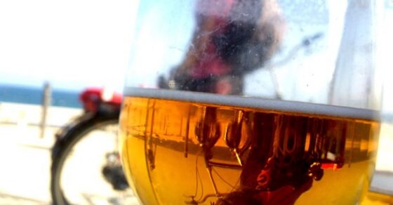 Copa de cerveza en primer plano en una terraza, con una bicicleta y el mar al fondo