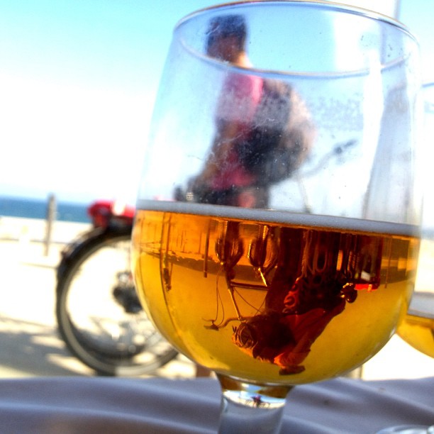 Copa de cerveza en primer plano en una terraza, con una bicicleta y el mar al fondo