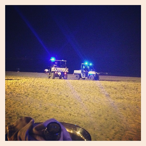 Dos vehículos de policía con las luces azules encendidas sobre la arena de una playa, de noche