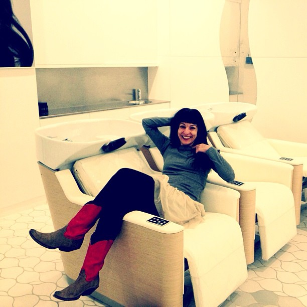 Mujer con botas rojas sonriendo, recostada en un sillón de lavacabezas blanco del nuevo espacio de L'Oréal en Barcelona
