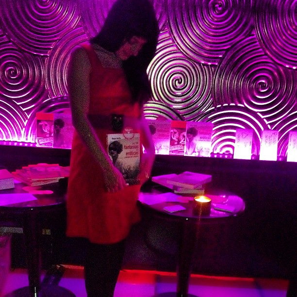 Roser Amills, con vestido rojo, junto a una mesa con ejemplares de Las 1001 fantasías en la sala Duvet, de luz violeta