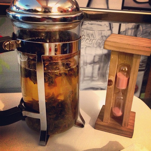 Cafetera de émbolo con té y reloj de arena de madera sobre una mesa
