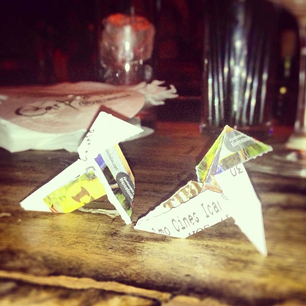 Dos pajaritas de papel hechas con hojas de periódico, sobre la barra de un bar