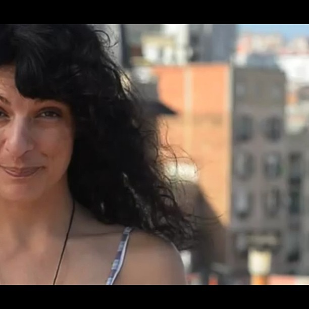 Primer plano de Roser Amills sonriendo, con el pelo al viento, ante edificios de una ciudad, en un fotograma de vídeo