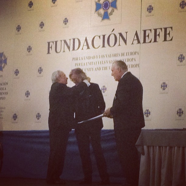 Entrega de una distinción a Víctor Amela ante el panel de la Fundación AEFE, entre dos hombres