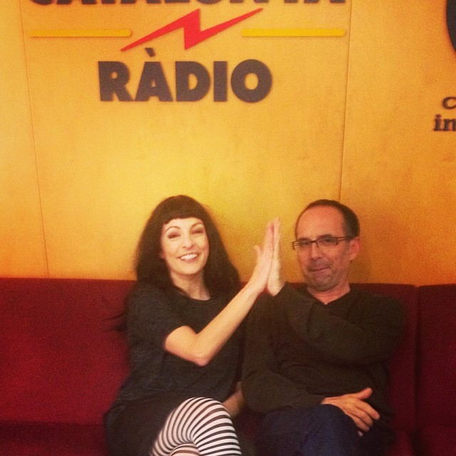 Roser Amills i Toni Orensanz xocant les mans en un sofà vermell davant el logotip de Catalunya Ràdio