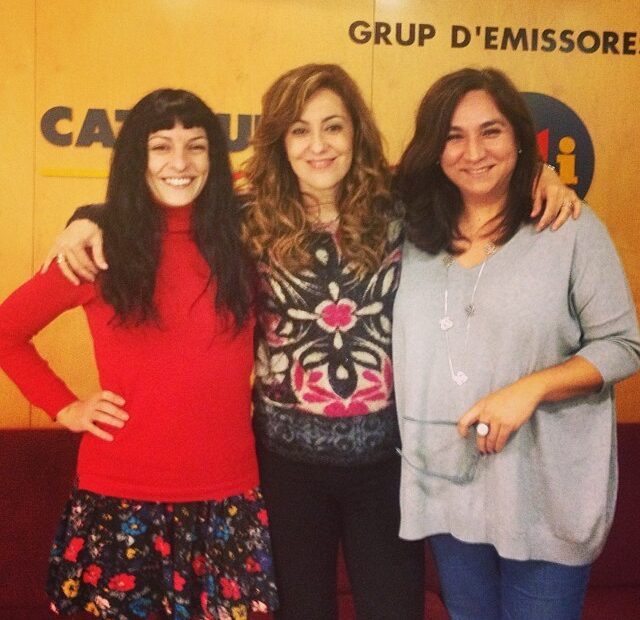 Roser Amills, amb jersei vermell, abraçada a dues dones davant el rètol de Catalunya Ràdio