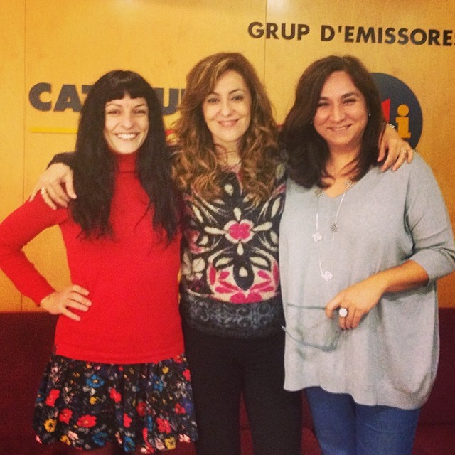 Roser Amills, amb jersei vermell, abraçada a dues dones davant el rètol de Catalunya Ràdio