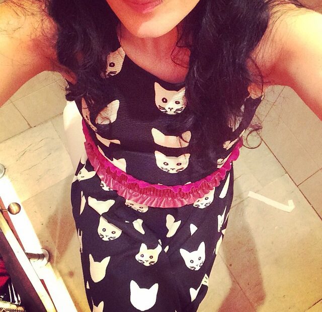 Torso de una mujer con un vestido negro estampado de caras de gato blancas y un cinturón rosa