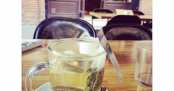 Una taza de té sobre una mesa, con la puerta acristalada de una cafetería al fondo