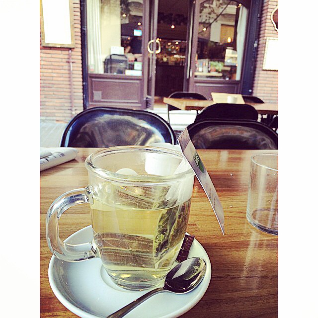 Una taza de té sobre una mesa, con la puerta acristalada de una cafetería al fondo