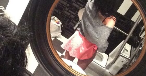 Reflejo en un espejo redondo de una mujer con falda rosa en unos baños con paredes a rayas blancas y negras