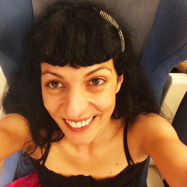 Selfi sonriente de Roser Amills con diadema en el pelo, sentada en el tren con un top negro