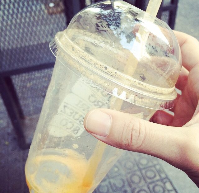 Vaso de plástico con tapa y pajita, casi vacío, con restos de zumo, sostenido en la mano