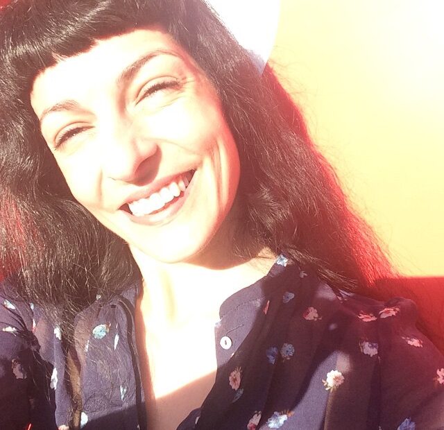 Selfi d'una dona que somriu amb el cabell fosc i serrell, il·luminada pel sol