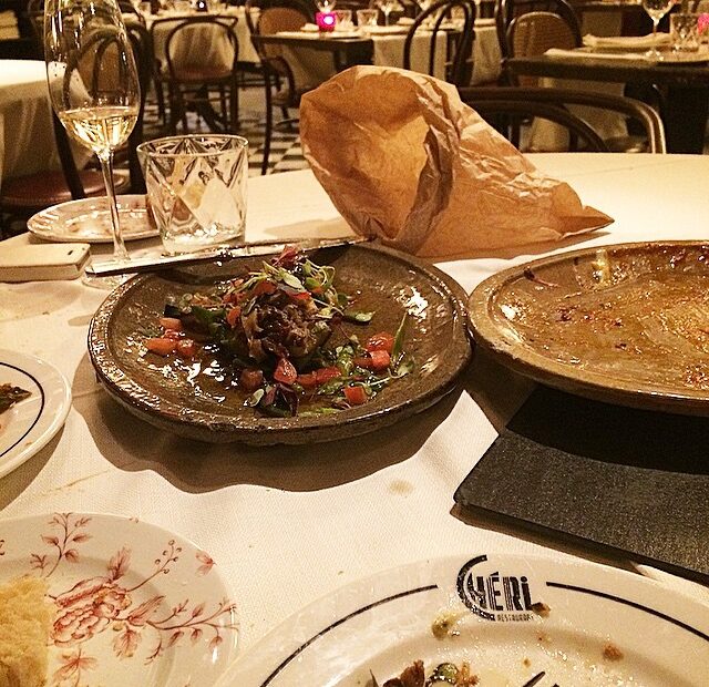 Mesa de restaurante con platos casi vacíos, una copa y una bolsa de papel