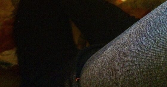 Piernas con medias negras y pantalón gris con los pies en alto sobre una silla, en la penumbra
