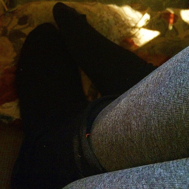 Piernas con medias negras y pantalón gris con los pies en alto sobre una silla, en la penumbra