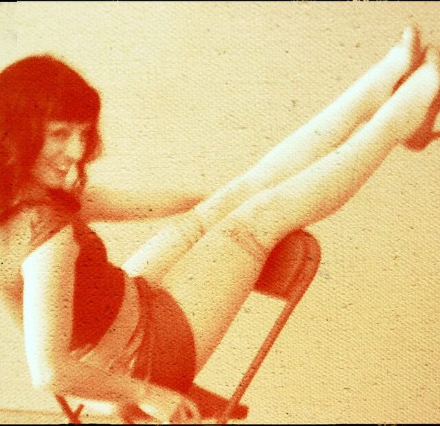 Roser Amills sentada en una silla plegable con las piernas levantadas, en una fotografía de tonos rojizos y aire retro